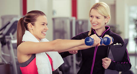 a female  personal trainer instructing a female client in a gym while she holds weights