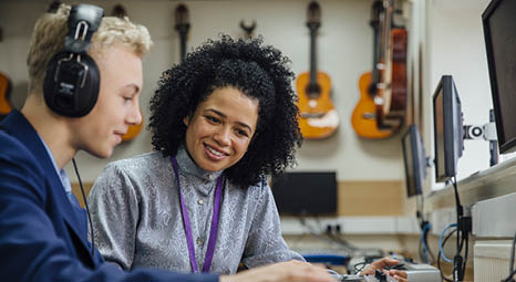 an lady teaching a student wearing headphones how to play on a keyboard